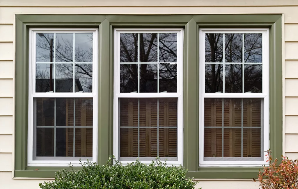 Three new replacement windows with green trim on front of house. Horizontal.