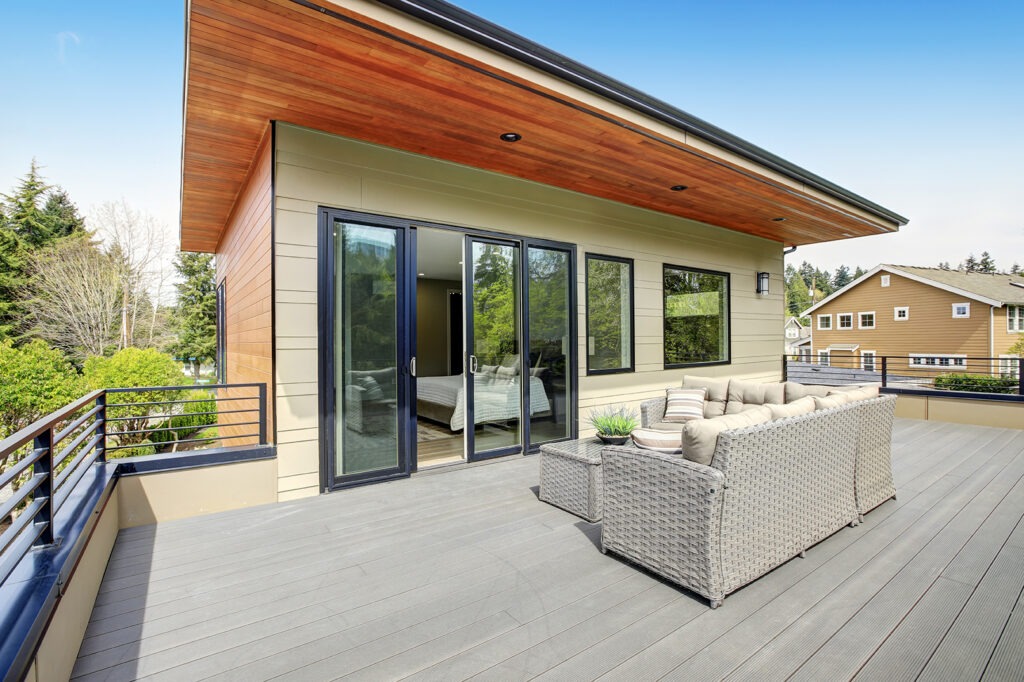 Contemporary deck features a modern wicker sectional facing glass sliding doors of a master bedroom .