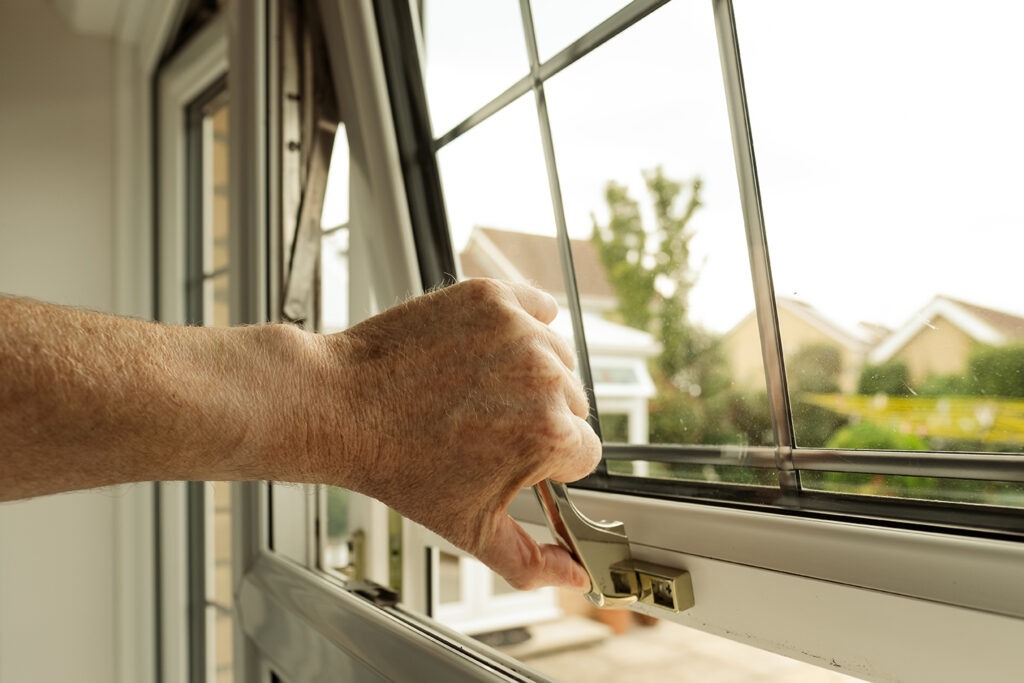 Homeowner seen about to lock a double glazed window seen on the ground level of a property. The latch can itself be locked to enhance security.