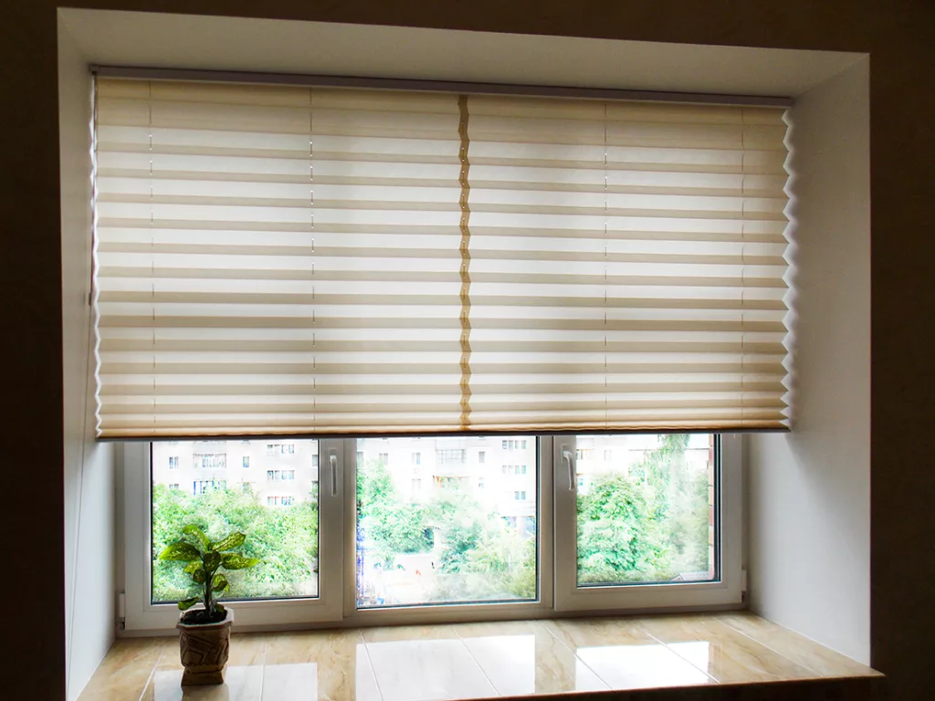 Pleated blinds XL Coulisse, beige color, with 50mm fold closeup in the window opening in the interior. Home blinds - modern bottom up privacy shades half raised on apartment windows.