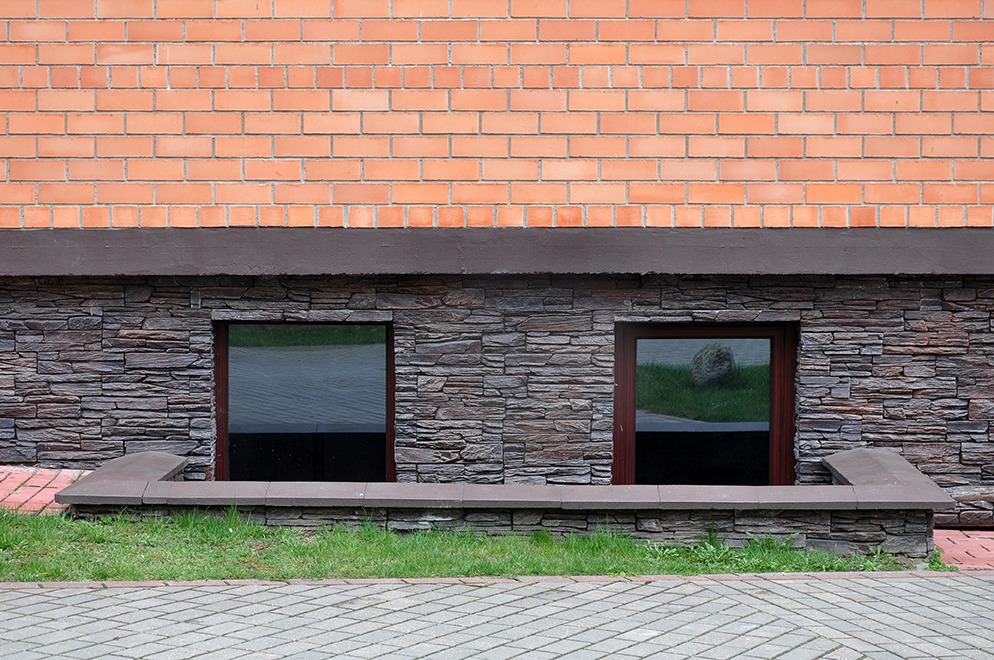 The basement of the brick building faced with natural stone with a pit and windows.