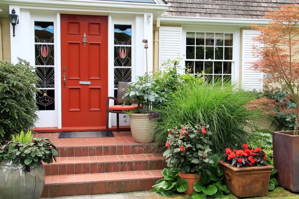 Charming small home with red front door and summer garden containers filled with annual flowers. Photo taken from the public sidewalk.