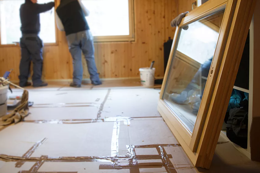 Workers in the background installing new, three pane wooden windows in an old wooden house, with a new window in the foreground. Home renovation, sustainable living, energy efficiency concept.